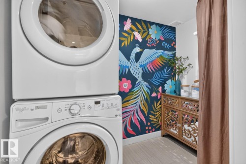 Stackable laundry appliances accompanied by a vibrant wall mural - 207 5025 Edgemont Boulevard, Edmonton, AB 