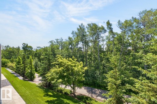 Expansive green space featuring a manicured lawn, established trees, and a paved pathway - 207 5025 Edgemont Boulevard, Edmonton, AB 