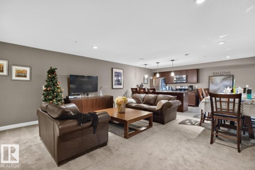 Open-concept living space featuring a kitchen with dark wood-finish cabinetry, stainless steel appliances, and pendant lighting - 207 5025 Edgemont Boulevard, Edmonton, AB 