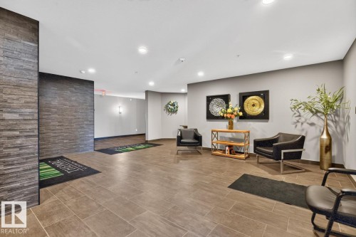 Spacious common area featuring large format tile flooring, a stacked stone accent wall, recessed lighting, and neutral wall tones - 207 5025 Edgemont Boulevard, Edmonton, AB 