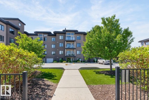 Modern multi-story building featuring contemporary architecture, multiple balconies with glass railings, and a clean concrete pathway entry - 207 5025 Edgemont Boulevard, Edmonton, AB 