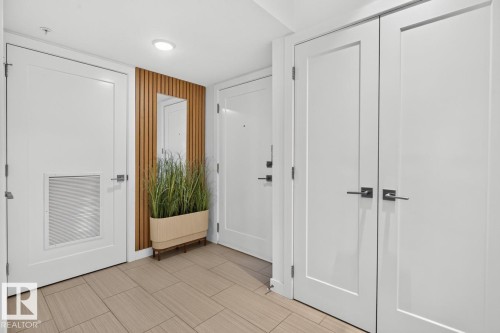 Entryway featuring rectangular tile flooring and a vertical wood slat accent wall with an integrated mirror - 207 5025 Edgemont Boulevard, Edmonton, AB 