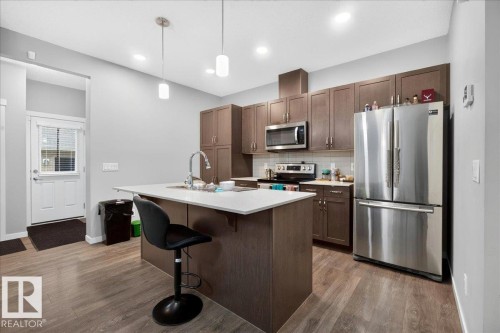 Open-concept kitchen featuring wood-finish flooring and a white front entry door - 1187 Cy Becker Road, Edmonton, AB 