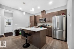 Open-concept kitchen featuring wood-finish flooring and a white front entry door - 