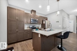 Modern kitchen featuring extensive wood-finish cabinetry, stainless steel appliances, a white tile backsplash, and a central island with a light-colored countertop - 