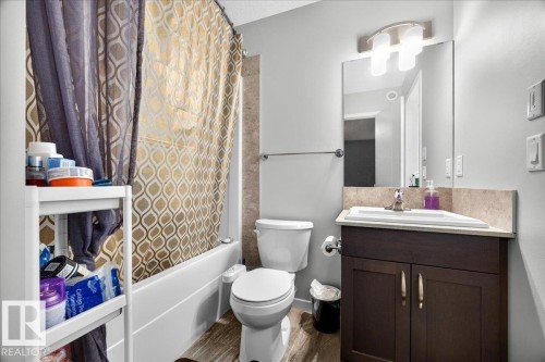 Bathroom featuring a white bathtub with tile surround, wood-finish flooring, a contemporary vanity with a white rectangular sink, a light-colored countertop, and a wall-mounted mirror with an overhead light fixture - 1187 Cy Becker Road, Edmonton, AB 