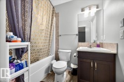 Bathroom featuring a white bathtub with tile surround, wood-finish flooring, a contemporary vanity with a white rectangular sink, a light-colored countertop, and a wall-mounted mirror with an overhead light fixture - 