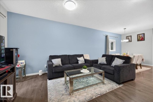 Open-concept living area featuring wood-finish flooring, light blue wall finishes, and a contemporary ceiling light fixture - 1187 Cy Becker Road, Edmonton, AB 