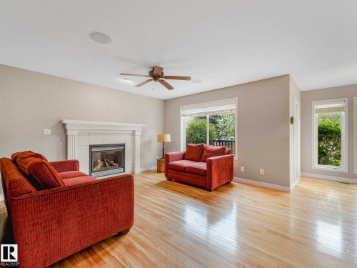 Living area featuring light wood-finish flooring, a white mantel fireplace with tile surround, multiple windows, a ceiling fan, and a built-in ceiling speaker - 1325 Latta Crescent, Edmonton, AB - Indoor Photo Showing Living Room With Fireplace