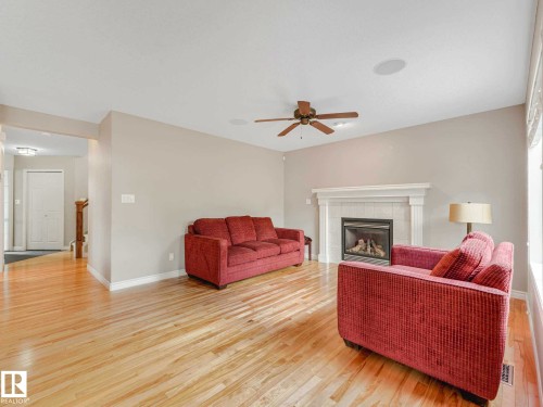 Bright living area featuring wood-finish flooring, a built-in gas fireplace with white mantel, a ceiling fan, and recessed ceiling speakers - 1325 Latta Crescent, Edmonton, AB - Indoor Photo Showing Living Room With Fireplace