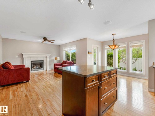 Open-concept living area featuring light wood-finish flooring, a prominent fireplace with a white mantel, and large windows providing ample natural illumination - 1325 Latta Crescent, Edmonton, AB - Indoor Photo Showing Living Room With Fireplace