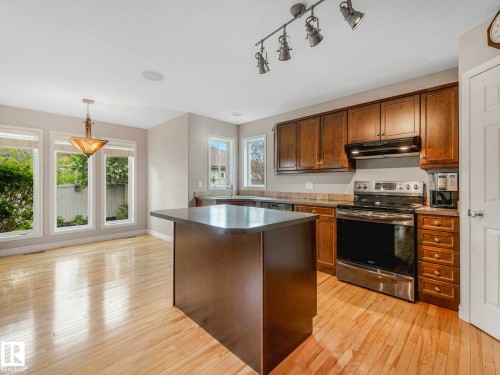 Kitchen featuring an island with a solid surface countertop, stainless steel appliances, wood-finish flooring, and ample natural light from multiple windows - 1325 Latta Crescent, Edmonton, AB - Indoor Photo Showing Kitchen With Double Sink