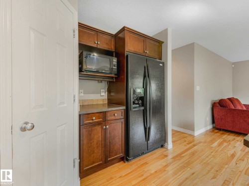 Kitchenette featuring wood cabinetry, stone-look countertop, integrated microwave, and a black side-by-side refrigerator - 1325 Latta Crescent, Edmonton, AB - Indoor