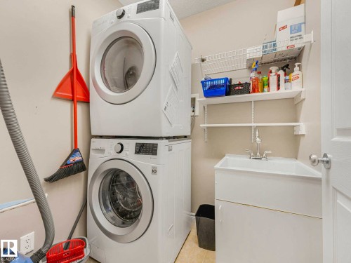 Dedicated laundry area featuring stacked front-load machines, a utility sink with a chrome faucet, and integrated wall shelving for organization - 1325 Latta Crescent, Edmonton, AB - Indoor Photo Showing Laundry Room