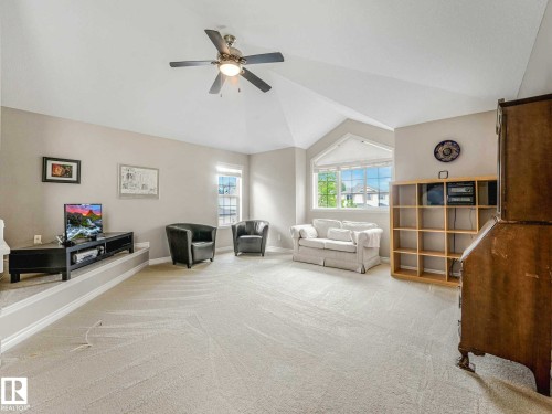 Spacious carpeted room featuring a vaulted ceiling with a ceiling fan, multiple windows providing natural light, and a raised platform - 1325 Latta Crescent, Edmonton, AB - Indoor