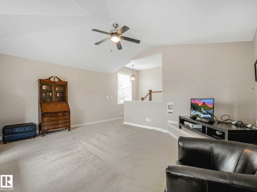 Spacious carpeted room featuring a ceiling fan with integrated lighting, neutral wall tones, and an open architectural feature overlooking a lower level with a visible staircase and pendant lighting - 1325 Latta Crescent, Edmonton, AB - Indoor
