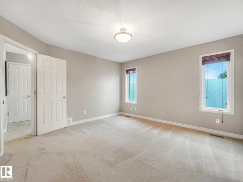 Spacious room featuring neutral carpeting, light gray walls, white trim, and two windows - 1325 Latta Crescent, Edmonton, AB - Indoor Photo Showing Other Room