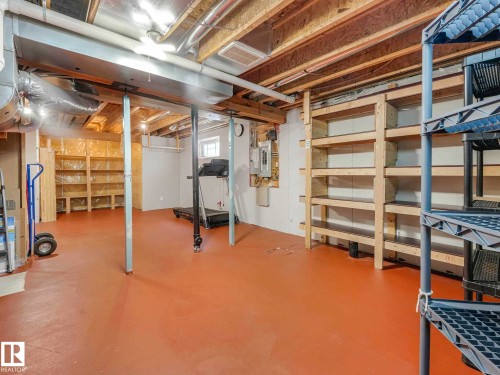 Spacious basement featuring painted concrete flooring, exposed ceiling joists, utility piping, and extensive built-in wooden shelving for storage - 1325 Latta Crescent, Edmonton, AB - Indoor Photo Showing Basement