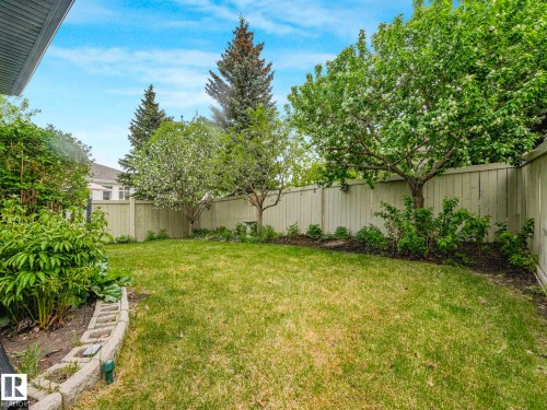 Fenced backyard featuring a manicured lawn, established trees, and perimeter garden beds with concrete block edging - 1325 Latta Crescent, Edmonton, AB - Outdoor With Backyard