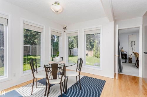 Dining area featuring multiple large windows, wood-finish flooring, a contemporary ceiling light fixture, and a doorway opening to another room - 11023 11A Avenue, Edmonton, AB 