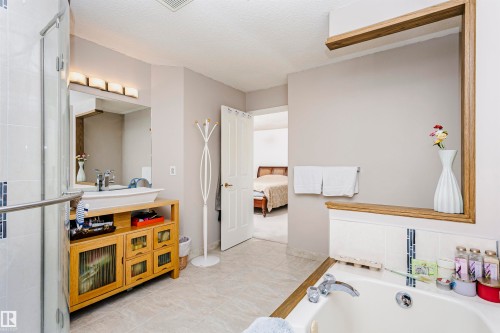 Bathroom featuring a soaker tub with tile surround, glass-enclosed shower, a wood-finish vanity with vessel sink, and an integrated wood-frame shelving unit - 11023 11A Avenue, Edmonton, AB 