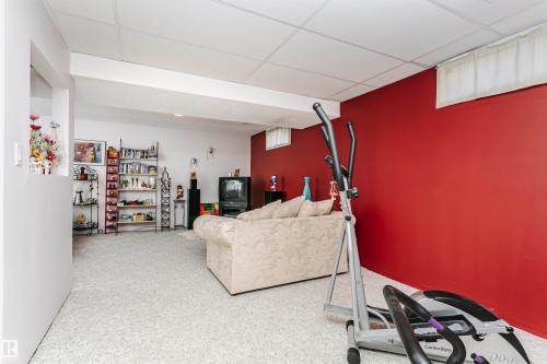 Carpeted lower level room featuring a drop-tile ceiling and a partial wall opening - 11023 11A Avenue, Edmonton, AB 