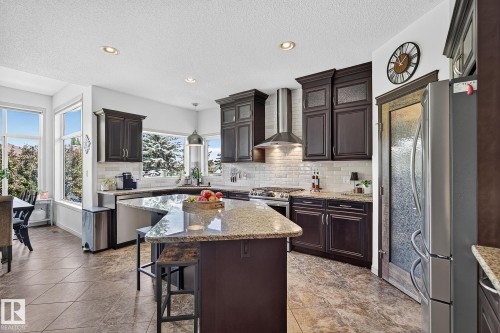 Spacious kitchen featuring dark wood cabinetry, light granite countertops, a large island with seating, stainless steel appliances, and tile flooring - 163 Galland Crescent, Edmonton, AB 