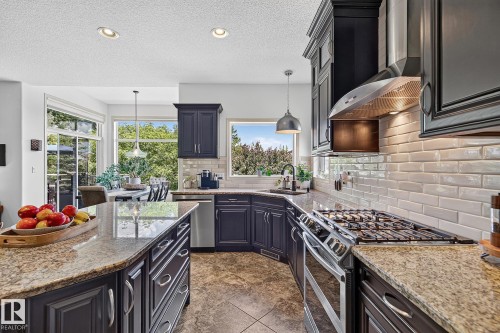 Kitchen featuring dark cabinetry, granite countertops, stainless steel appliances, and a subway tile backsplash - 163 Galland Crescent, Edmonton, AB 