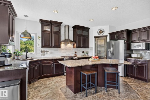 Kitchen featuring dark wood cabinetry, light granite countertops, a large center island, stainless steel appliances, and wood-finish flooring - 163 Galland Crescent, Edmonton, AB 