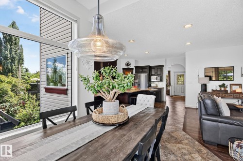Open-concept living area featuring a formal dining space with a large window and a contemporary glass pendant light fixture - 163 Galland Crescent, Edmonton, AB 