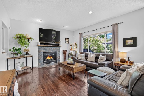 Living area featuring a stone-clad fireplace, wood-finish flooring, recessed lighting, and a large window - 163 Galland Crescent, Edmonton, AB 