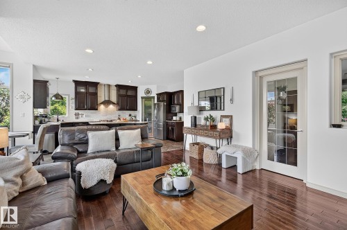 Open-concept living area featuring rich wood-finish flooring, recessed lighting, white walls, and a multi-panel glass door - 163 Galland Crescent, Edmonton, AB 