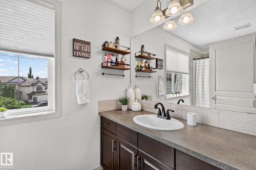 White double-paned window with horizontal blinds, dark wood-finish vanity with a single basin sink, matte black faucet, and a textured backsplash - 163 Galland Crescent, Edmonton, AB 
