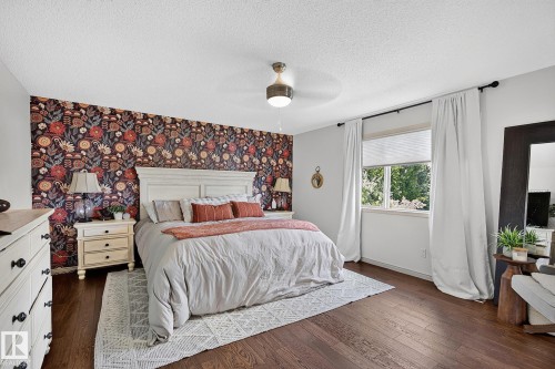Bedroom featuring a decorative accent wall, wood-finish flooring, a ceiling fan with integrated lighting, and a large window with privacy blinds and drapes - 163 Galland Crescent, Edmonton, AB 