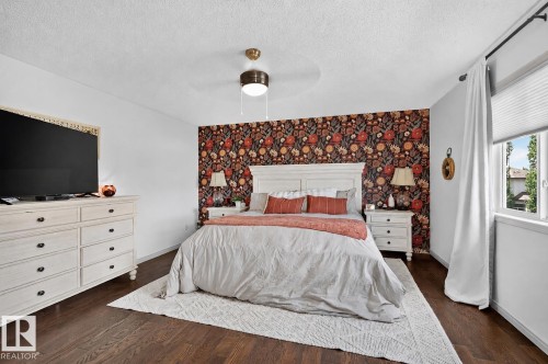 Bedroom featuring a statement wall with botanical wallpaper, rich wood-finish flooring, and a ceiling fan with integrated lighting - 163 Galland Crescent, Edmonton, AB 