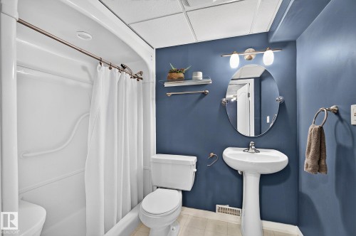 Bathroom featuring a single-piece shower-tub combination, pedestal sink, and oval mirror - 163 Galland Crescent, Edmonton, AB 
