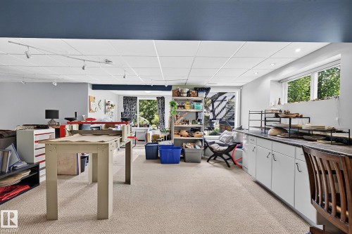 Spacious lower-level room featuring an egress window, track lighting, recessed lighting, white cabinetry with dark countertops, and light-toned carpet flooring - 163 Galland Crescent, Edmonton, AB 