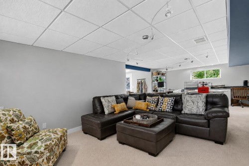 Spacious recreational room featuring light-colored carpeting, a grid drop ceiling with track lighting, and a window with exterior views - 163 Galland Crescent, Edmonton, AB 