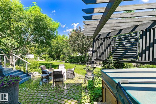 Expansive backyard featuring a large lawn area, mature trees, a ground-level patio with grid pavers, and a covered pergola structure - 163 Galland Crescent, Edmonton, AB 