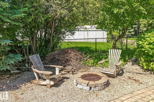 Outdoor fire pit area featuring a stone block fire pit, gravel ground cover, and surrounding mature trees - 163 Galland Crescent, Edmonton, AB 
