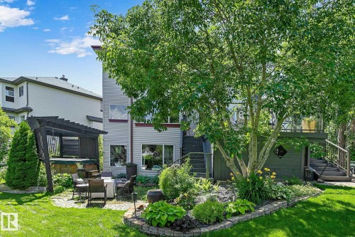 Expansive backyard featuring a manicured lawn, established tree, and a stone-paved patio with a dark wood pergola - 163 Galland Crescent, Edmonton, AB 