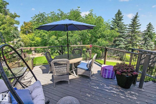 Expansive outdoor deck featuring dark wood-finish flooring, dark metal railings, and mature surrounding greenery - 163 Galland Crescent, Edmonton, AB 