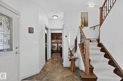 Entryway featuring a decorative glass-paneled door, natural wood staircase with wrought iron balusters, and carpeted treads - 163 Galland Crescent, Edmonton, AB 