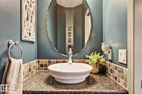 Powder room featuring a vessel sink, polished chrome faucet, stone-finish countertop, and decorative tile backsplash - 163 Galland Crescent, Edmonton, AB 