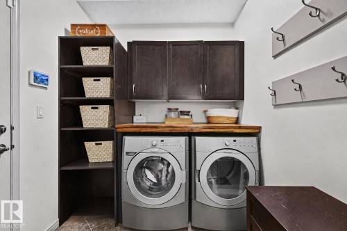 Functional laundry area featuring built-in shelving, dark wood-finish cabinetry, and a wood-finish countertop - 163 Galland Crescent, Edmonton, AB 