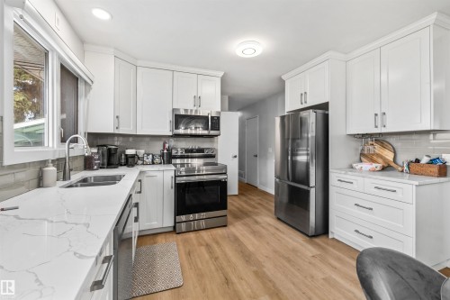 Modern kitchen featuring white shaker cabinetry, stainless steel appliances, marble-look countertops, a light gray tile backsplash, and light wood-finish flooring - 10130 62 Street, Edmonton, AB - Indoor Photo Showing Kitchen With Double Sink With Upgraded Kitchen