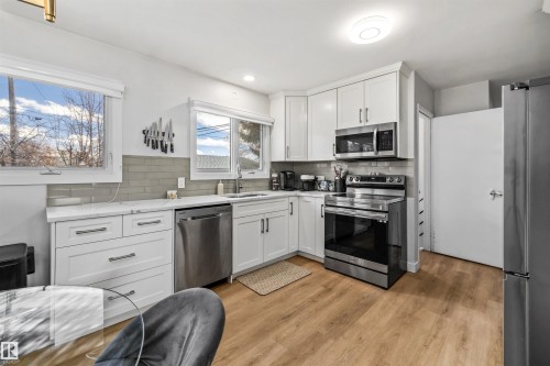 Kitchen featuring white cabinetry, light-toned wood-finish flooring, stainless steel appliances, and a tile backsplash - 10130 62 Street, Edmonton, AB - Indoor Photo Showing Kitchen With Upgraded Kitchen