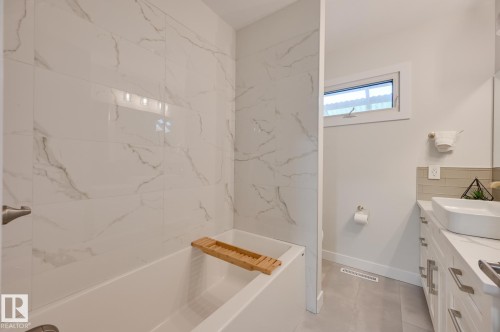 Bathroom featuring a white bathtub with full-height marble-effect tile surround - 10130 62 Street, Edmonton, AB - Indoor Photo Showing Bathroom