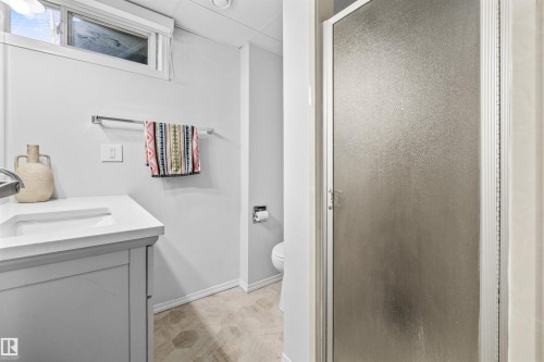 Bathroom featuring a white vanity with integrated sink, patterned floor tiles, and a frosted glass shower enclosure - 10130 62 Street, Edmonton, AB - Indoor Photo Showing Bathroom