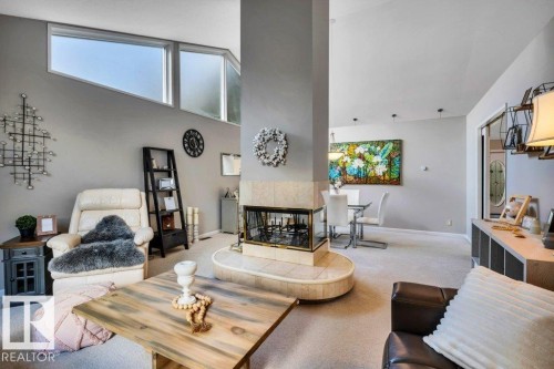 Living area featuring a central fireplace with stone surround, a vaulted ceiling, and high-set windows - 11742 29 Avenue, Edmonton, AB 